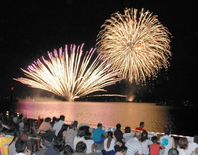 打ち上げ花火と水中仕掛け花火の競演を楽しむ見物客（資料）