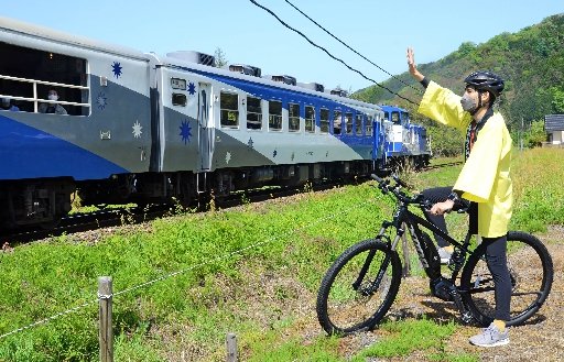 自転車に乗ってトロッコ列車「奥出雲おろち号」に手を振る雲南市観光協会の職員＝雲南市木次町寺領