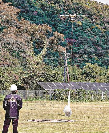 飲料水の入った箱をつり下げながら飛び立つ大型ドローン＝島根県美郷町簗瀬、吾郷公民館
