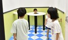 体が消えて見える仕掛けが施された装置で遊ぶ子どもたち＝松江市袖師町、県立美術館