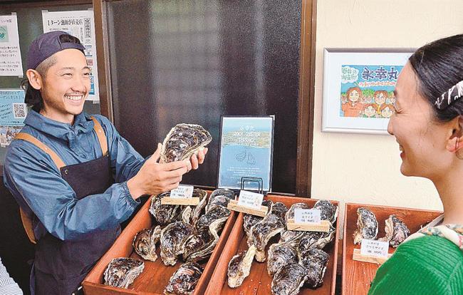 オープンした直売所で来店客（右）にイワガキを薦める永見輝晃さん＝松江市島根町野井