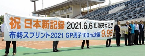 横断幕を掲げ、日本記録樹立を祝う陸上競技関係者＝鳥取市布勢、ヤマタスポーツパーク陸上競技場