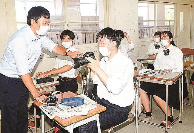 写真の撮り方講座で、山陰中央新報社邑南通信部の糸賀淳也記者（左）が実際に取材に使っているカメラを手に取る生徒（中央）＝江津市都野津町、江津高校