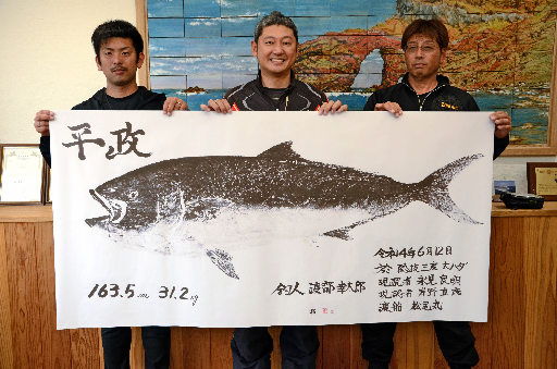 巨大ヒラマサの魚拓を持つ、左から松尾翔平さん、渡部幸太郎さん、永見良明さん＝島根県西ノ島町美田、町役場