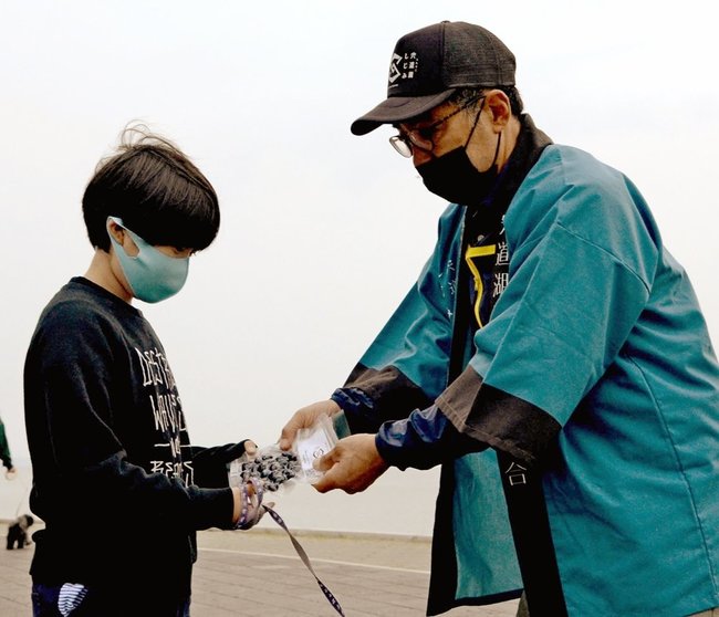 真空パックのシジミを手渡す宍道湖漁業組合の福間弘幸さん（右）＝松江市袖師町、岸公園