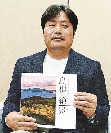 島根県内の美しい風景を収めた写真集「島根絶景」を手にする写真家のＫＷＡＮさん＝松江市殿町、県庁