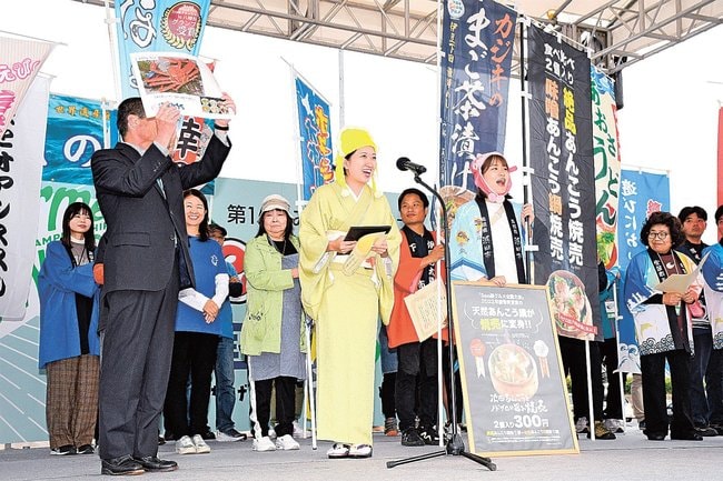 ステージ上で祝福されて笑顔を見せる、みなとオアシス浜田の増田可夏子さん(前列左から2人目)と竹林優花さん(同3人目)=境港市竹内団地、境夢みなとターミナル駐車場の特設ステージ