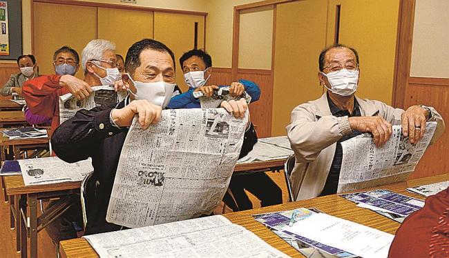 新聞紙を指先だけで巻き上げる参加者＝出雲市佐田町大呂、大呂交流会館