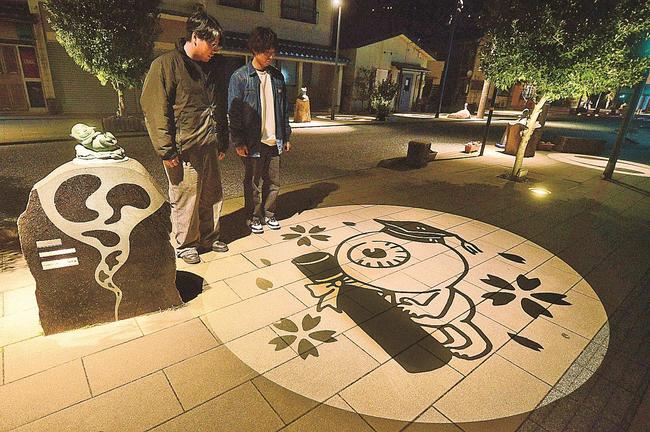 帽子をかぶり、賞状筒を手にした目玉おやじの妖怪影絵に見入る観光客＝境港市大正町
