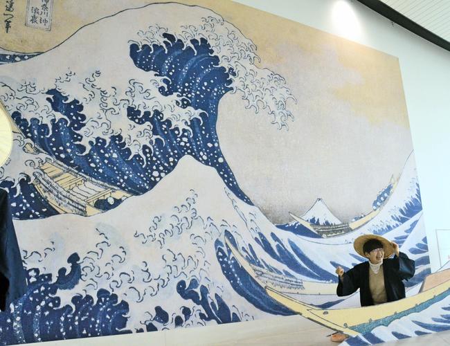 「神奈川沖浪裏」の拡大パネルの前で笠をかぶって写真に収まる来館者＝２０１９年、島根県立美術館