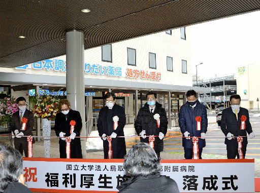 テープカットする関係者。後方が完成した福利厚生施設棟=米子市西町、鳥取大医学部付属病院