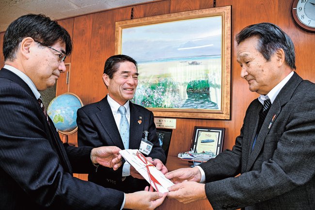 佐篠邦雄会長（右）に収益金を手渡す伊達憲太郎市長（中央）と藤井満弘執行役員米子総局長＝境港市上道町、市役所