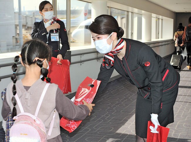 乗客に、特製のあめを配る日本航空の客室乗務員（右）＝東京都大田区、羽田空港