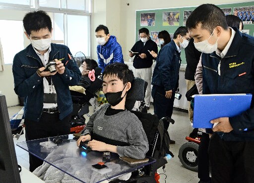 生徒(中央)が握るコントローラーを視察する松江工業高等専門学校の職員=松江市上乃木5丁目、松江緑が丘養護学校