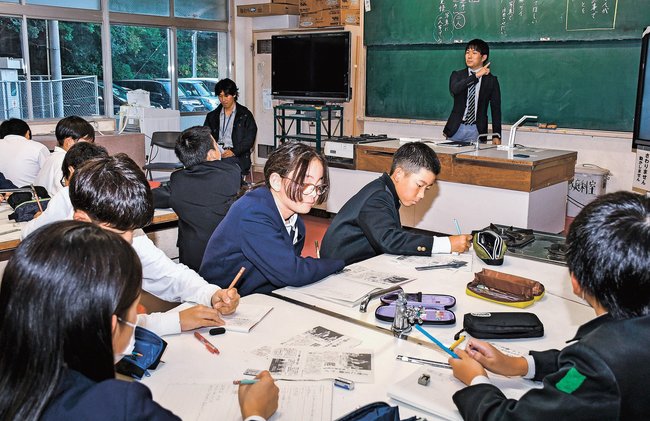 記事の工夫を交えた清山遼太記者（右奥）の話を聞く児童＝松江市八幡町、竹矢小学校