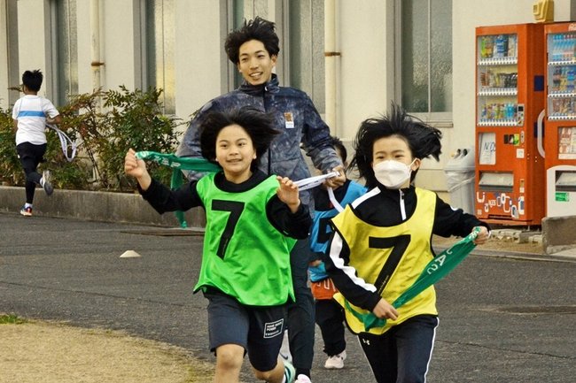 三浦龍司選手（中央奥）と一緒に走る子どもたち＝島根県浜田市黒川町、市陸上競技場前広場