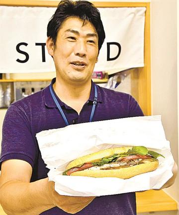 「鯖ドッグ」を手にする三島淳寛社長＝浜田市原井町、山陰浜田港公設市場