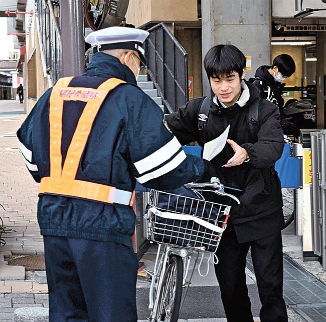 自転車のヘルメット着用を呼びかけるチラシを受け取る市民（右）＝松江市朝日町、ＪＲ松江駅西駐輪場前