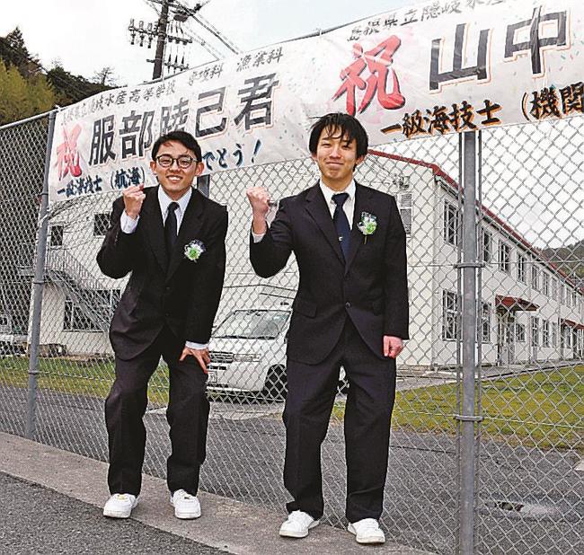 横断幕の前で合格を喜ぶ服部睦己さん（左）と山中勇輝さん＝島根県隠岐の島町東郷、隠岐水産高校