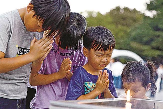 平和記念公園で手を合わせる子どもたち＝６日、広島市