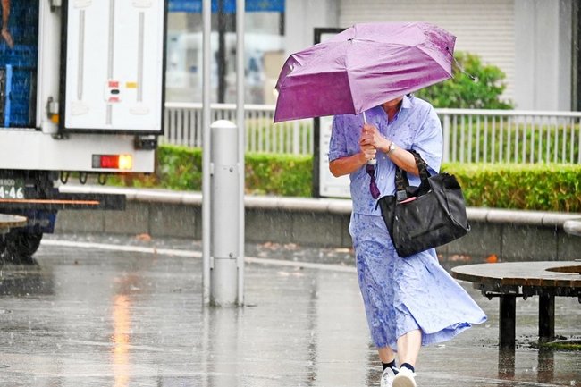 激しい雨と強風に傘を握る歩行者＝３０日午後４時２分、松江市朝日町、ＪＲ松江駅前