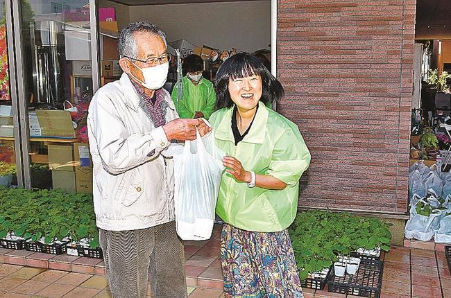 来場者（左）にゴーヤーの苗を手渡す益田法人会員＝益田市駅前町、フラワー湖月