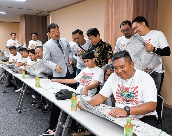 バリ島マス村からの島根県美郷町訪問を報じた本紙を眺めるダルマユダ村長（手前）ら∥松江市殿町、山陰中央新報社