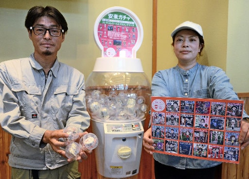 大森雄介さん（左）らが設置したご当地ガチャ。池田佳奈さんが手にするシートに描かれた２３種類のシールが入っている＝安来市安来町、市観光交流プラザ