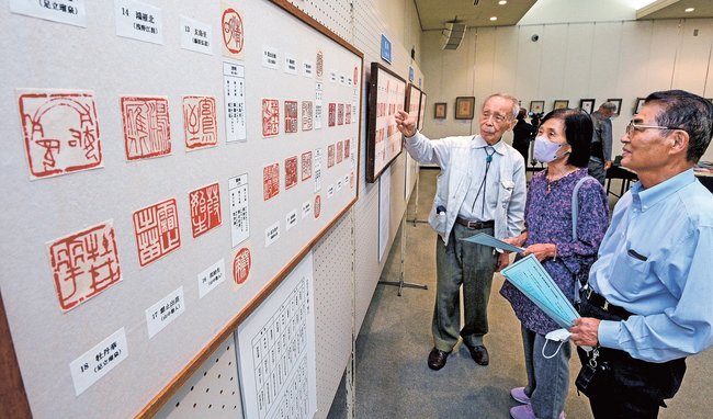 会員（左）の説明を聞きながら篆刻作品を楽しむ来場者＝松江市殿町、島根県民会館