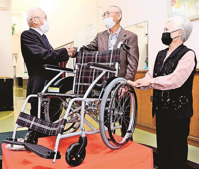 田中敏勝理事長（左）に車椅子を渡す野田政利さん、美恵さん夫婦＝浜田市西村町、養護老人ホーム松風園