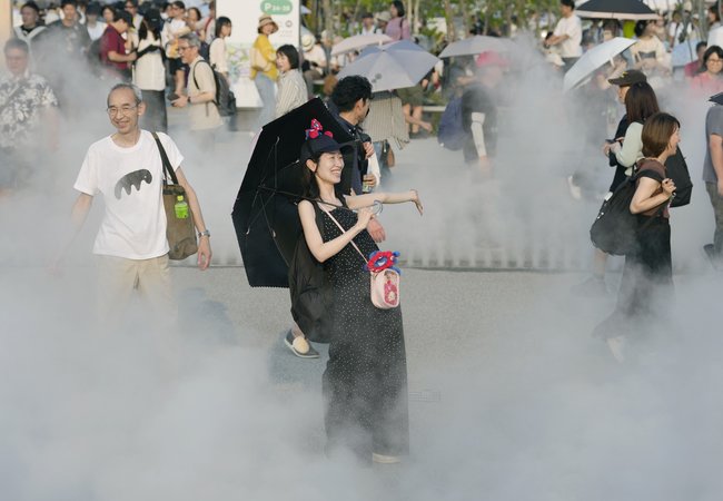 梅雨明けの強い日差しの中、大阪・関西万博会場で日傘を差しミストを浴びる来場者＝６月２７日、大阪市此花区の夢洲