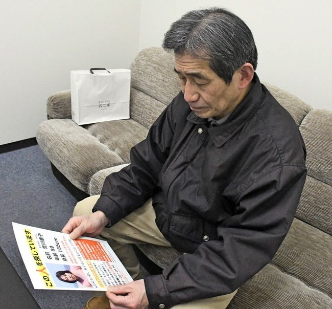 荒川泰子さんの情報を呼びかけるポスターを見つめる夫の勉さん＝松江市内