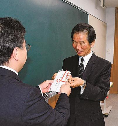 松江市保育研究会の国頭正久会長（左）に図書カードの目録を手渡す東雲会の青山龍太郎会長＝松江市東津田町、いきいきプラザ島根