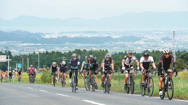中海が見渡せる絶景を背後にペダルをこぐ参加者=鳥取県伯耆町丸山