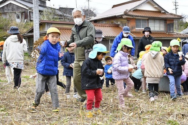 白クローバーの種を混ぜた砂を羊放牧場予定地にまく子どもたち＝江津市波子町