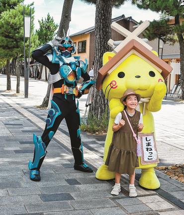 神門通りで観光客とポーズを決める仮面ライダーガッチャード（左）としまねっこ＝出雲市大社町杵築南