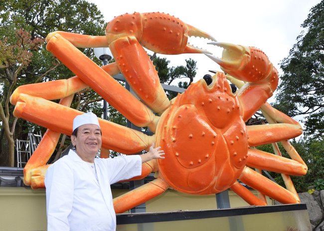 すし博多の看板、巨大なカニの置物を前にほほ笑む永瀬豊代表