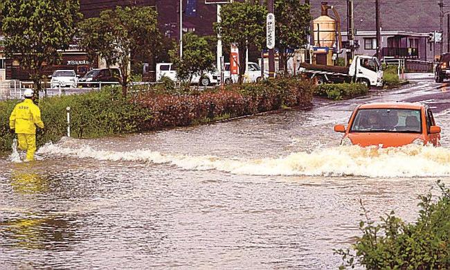 水しぶきを上げ、冠水した国道４３２号を走る車＝７日、松江市八雲町東岩坂