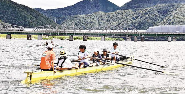 江津工高ボート部員と息を合わせてオールを動かす児童＝江津市江津町、江の川河口