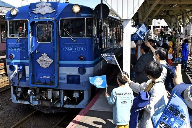 小旗を振り、観光列車「あめつち」を歓迎する沿線住民ら＝雲南市木次町里方、ＪＲ木次駅