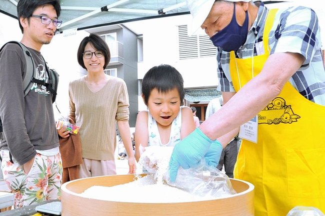 子ども食堂のブースで、もち米のすくい取りに挑戦する来場者＝松江市殿町、南殿町商店街