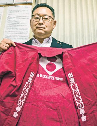 現地で着る「出雲ぜんざい学会」の法被とともにＰＲに意気込む渡部稔会長＝出雲市大社町北荒木、出雲観光タクシー