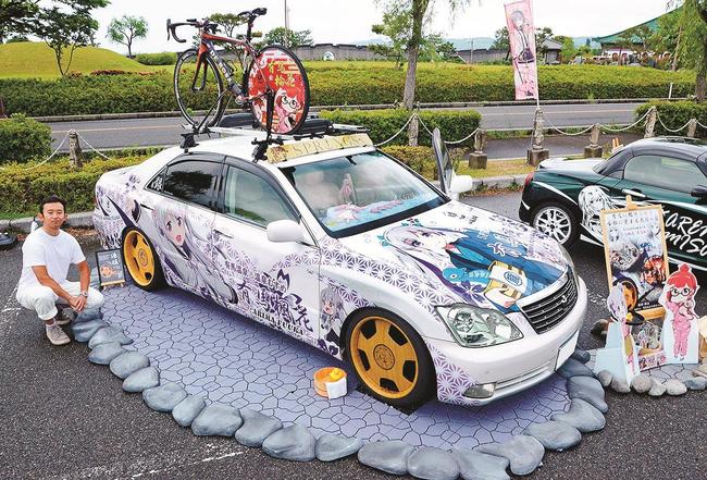 有馬温泉の温泉むすめ「有馬楓花」を描いた痛車とオーナー。屋根には「有馬輪花」を描いた自転車が載る=鳥取県湯梨浜町引地、道の駅燕趙園(画像の一部を加工しています)