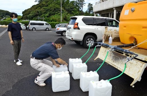 給水所に持ち込まれたポリタンクに水を注ぐ出雲市職員（手前）＝１９日午前１１時３分、出雲市多伎町小田、市多伎行政センター