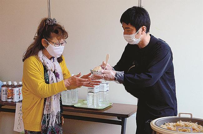 炊き出しのアワビご飯を受け取る避難者（左）＝松江市島根町加賀、島根公民館