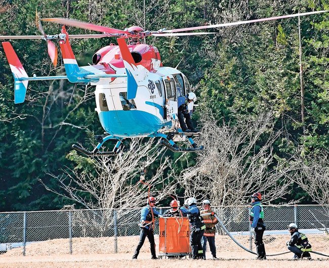 ヘリがつり上げるバケットに補水する消防署員ら＝益田市美都町都茂、美都運動場