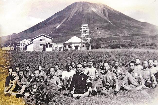 大山の麓にあった滑空訓練所で少年航空兵を目指した２期生の一部と教官（正面）ら。後方の建物は滑空機の倉庫や事務本部、宿舎棟などだった（１９４４年８月撮影、宇田川潔さん提供）