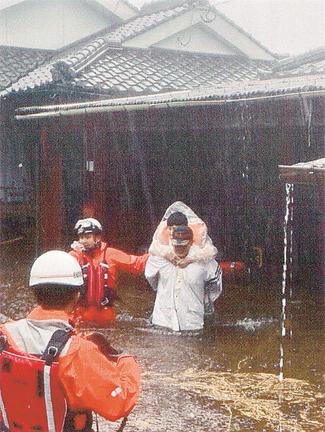 鹿児島県伊佐市で床上浸水した住宅に取り残された８０代女性を背負って救助する警察官＝１０日午前（同県警提供）