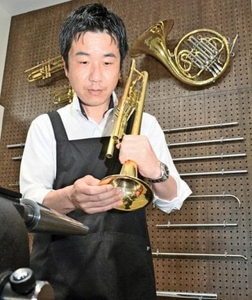 壁に工具類が掛かる工房で楽器修理に取り組む板持信也さん