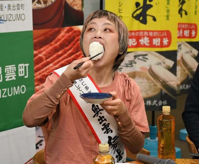 奥出雲仁多米大使を任命し、おにぎりを大口で頬張るロシアン佐藤さん=島根県奥出雲町三成、同町役場仁多庁舎
